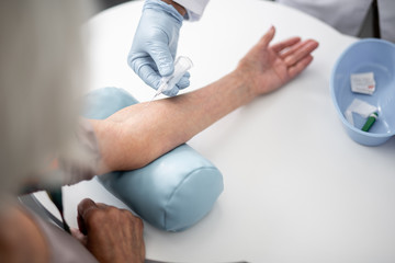 Professional doctor in rubber gloves using vacuum blood collection needle while working with patient