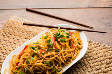 Schezwan Noodles or vegetable Hakka Noodles or chow mein is a popular Indo-Chinese recipes, served in a bowl or plate with wooden chopsticks. selective focus