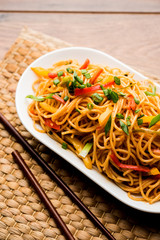Schezwan Noodles or vegetable Hakka Noodles or chow mein is a popular Indo-Chinese recipes, served in a bowl or plate with wooden chopsticks. selective focus