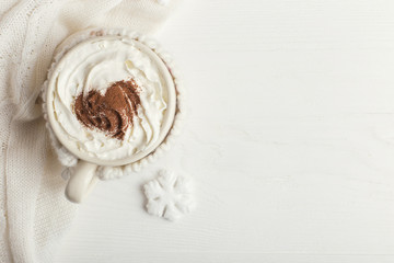 A cup of hot winter drink with whipped cream and a dusting powder with an asterisk, white snowflakes and knitted scarf on a wooden table. Christmas concept in bright colors. Copy space.