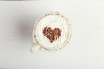 A cup of hot winter drink, with whipped cream and cocoa powder and white snowflakes on a wooden table. Christmas concept in bright colors. Copy space.