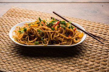 Schezwan Noodles or vegetable Hakka Noodles or chow mein is a popular Indo-Chinese recipes, served in a bowl or plate with wooden chopsticks. selective focus