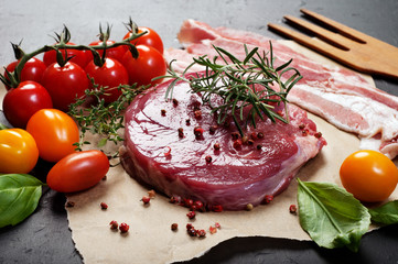 Raw meat (steak) on parchment paper. Next to the multicolored tomatoes and basil leaves. Macro shooting.
