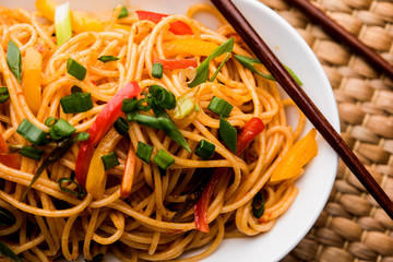 Schezwan Noodles or vegetable Hakka Noodles or chow mein is a popular Indo-Chinese recipes, served in a bowl or plate with wooden chopsticks. selective focus