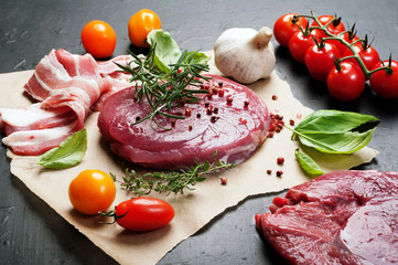 Raw meat (steak) on parchment paper. Next to the multicolored tomatoes and basil leaves. Macro shooting.