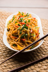 Schezwan Noodles or vegetable Hakka Noodles or chow mein is a popular Indo-Chinese recipes, served in a bowl or plate with wooden chopsticks. selective focus