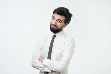 Smiling handsome hispanic man with black beard in white shirt crossing hands.