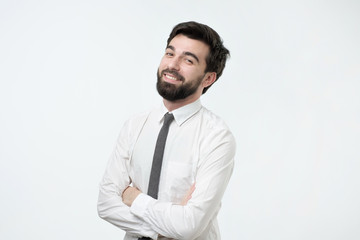 Smiling handsome hispanic man with black beard in white shirt crossing hands.