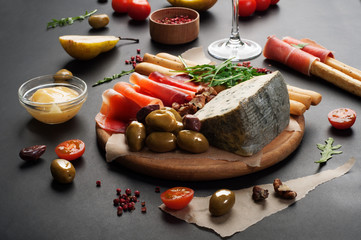 Mediterranean products (ham, blue cheese, arugula, cherry, nuts) on a brown cutting board. Dark background. Useful natural fresh food