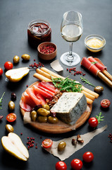 Fototapeta na wymiar Mediterranean products (ham, blue cheese, arugula, cherry, nuts) on a brown cutting board. Dark background. Useful natural fresh food