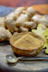 Fresh raw ginger root and bowl with ginger powder close up
