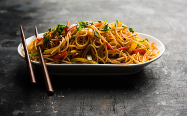 Schezwan Noodles or vegetable Hakka Noodles or chow mein is a popular Indo-Chinese recipes, served in a bowl or plate with wooden chopsticks. selective focus