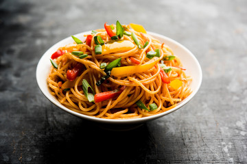 Schezwan Noodles or vegetable Hakka Noodles or chow mein is a popular Indo-Chinese recipes, served in a bowl or plate with wooden chopsticks. selective focus