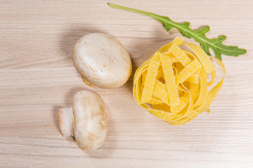 Pasta with mushrooms and arugula on light wooden table in restaurant. Ingredients on wooden background