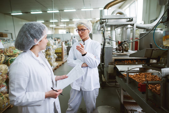 Two female workers discussing while standing in food factory.