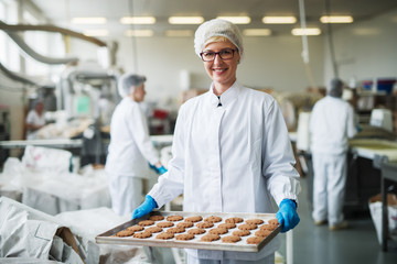 Female worker standing and holding plate with cookies.