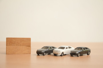 Black and white miniature car with wooden block on brown wood.