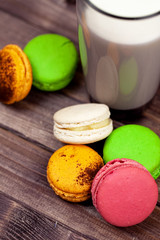 Multicolored macaroons and a glass of milk on a wooden table top view