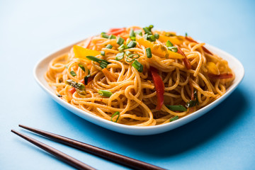 Schezwan Noodles or vegetable Hakka Noodles or chow mein is a popular Indo-Chinese recipes, served in a bowl or plate with wooden chopsticks. selective focus