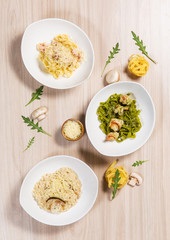 Pasta in white plates with different ingredients on light wooden table in a restaurant. Shrimps, arugula, mushrooms