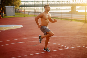 Fototapeta premium Fitness training outdoors. Handsome man working exercises in early morning with sunrise. Muscular man training outside. Sunny fitness morning.