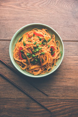 Schezwan Noodles or vegetable Hakka Noodles or chow mein is a popular Indo-Chinese recipes, served in a bowl or plate with wooden chopsticks. selective focus