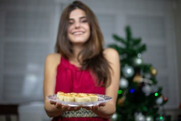 Blurred woman in dress offering Christmas marzipan treat on plate standing indoors 