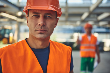 Close up of male employee of construction company is locating in hangar with his colleague on background