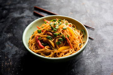 Schezwan Noodles or vegetable Hakka Noodles or chow mein is a popular Indo-Chinese recipes, served in a bowl or plate with wooden chopsticks. selective focus