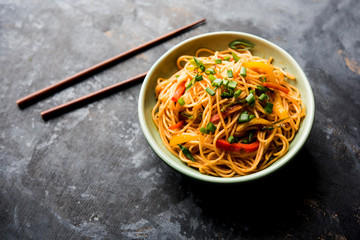 Schezwan Noodles or vegetable Hakka Noodles or chow mein is a popular Indo-Chinese recipes, served in a bowl or plate with wooden chopsticks. selective focus
