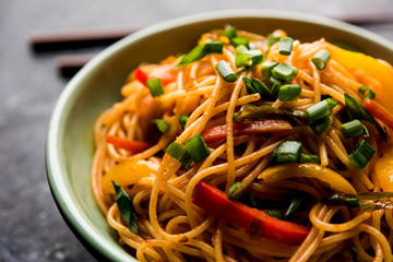Schezwan Noodles or vegetable Hakka Noodles or chow mein is a popular Indo-Chinese recipes, served in a bowl or plate with wooden chopsticks. selective focus