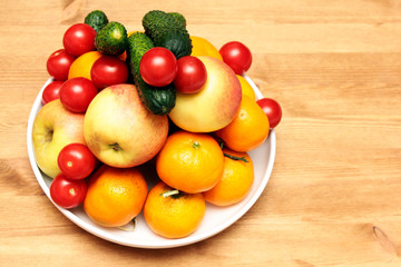 tomatoes, cucumbers, tangerines and apples on a wooden table on a plate