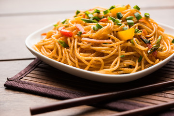 Schezwan Noodles or vegetable Hakka Noodles or chow mein is a popular Indo-Chinese recipes, served in a bowl or plate with wooden chopsticks. selective focus
