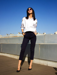 young sexy brunette girl with stylish hair and long legs in white shirt  is standing with hands in pockets and looking straight on the roof of the restaurant background, business lifestyle concept