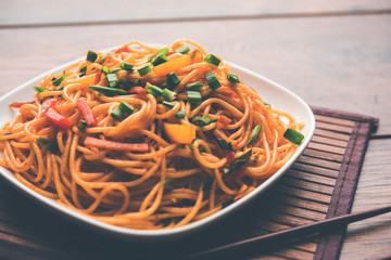 Schezwan Noodles or vegetable Hakka Noodles or chow mein is a popular Indo-Chinese recipes, served in a bowl or plate with wooden chopsticks. selective focus