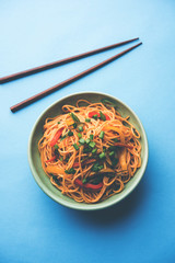 Schezwan Noodles or vegetable Hakka Noodles or chow mein is a popular Indo-Chinese recipes, served in a bowl or plate with wooden chopsticks. selective focus