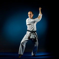 Fototapeta na wymiar An active athlete trains formal karate exercises on a blue tatami