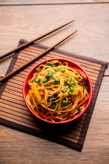Schezwan Noodles or vegetable Hakka Noodles or chow mein is a popular Indo-Chinese recipes, served in a bowl or plate with wooden chopsticks. selective focus