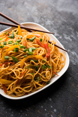 Schezwan Noodles or vegetable Hakka Noodles or chow mein is a popular Indo-Chinese recipes, served in a bowl or plate with wooden chopsticks. selective focus