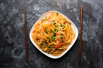 Schezwan Noodles or vegetable Hakka Noodles or chow mein is a popular Indo-Chinese recipes, served in a bowl or plate with wooden chopsticks. selective focus