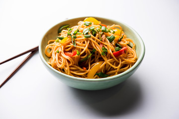 Schezwan Noodles or vegetable Hakka Noodles or chow mein is a popular Indo-Chinese recipes, served in a bowl or plate with wooden chopsticks. selective focus
