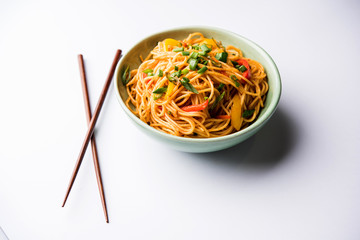 Schezwan Noodles or vegetable Hakka Noodles or chow mein is a popular Indo-Chinese recipes, served in a bowl or plate with wooden chopsticks. selective focus