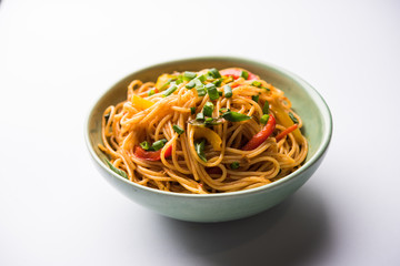 Schezwan Noodles or vegetable Hakka Noodles or chow mein is a popular Indo-Chinese recipes, served in a bowl or plate with wooden chopsticks. selective focus