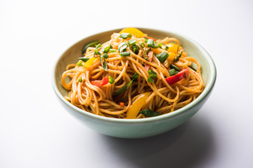 Schezwan Noodles or vegetable Hakka Noodles or chow mein is a popular Indo-Chinese recipes, served in a bowl or plate with wooden chopsticks. selective focus