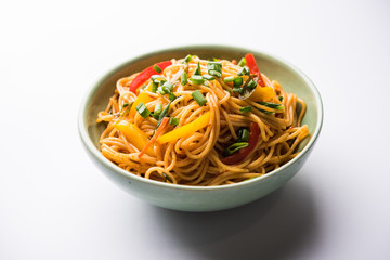 Schezwan Noodles or vegetable Hakka Noodles or chow mein is a popular Indo-Chinese recipes, served in a bowl or plate with wooden chopsticks. selective focus