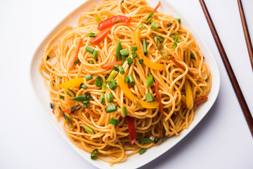 Schezwan Noodles or vegetable Hakka Noodles or chow mein is a popular Indo-Chinese recipes, served in a bowl or plate with wooden chopsticks. selective focus