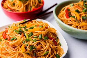Schezwan Noodles or vegetable Hakka Noodles or chow mein is a popular Indo-Chinese recipes, served in a bowl or plate with wooden chopsticks. selective focus