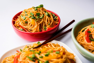 Schezwan Noodles or vegetable Hakka Noodles or chow mein is a popular Indo-Chinese recipes, served in a bowl or plate with wooden chopsticks. selective focus
