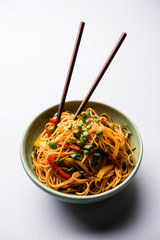 Schezwan Noodles or vegetable Hakka Noodles or chow mein is a popular Indo-Chinese recipes, served in a bowl or plate with wooden chopsticks. selective focus