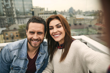 Waist up of happy man and woman is locating in terrace while making selfie in smartphone